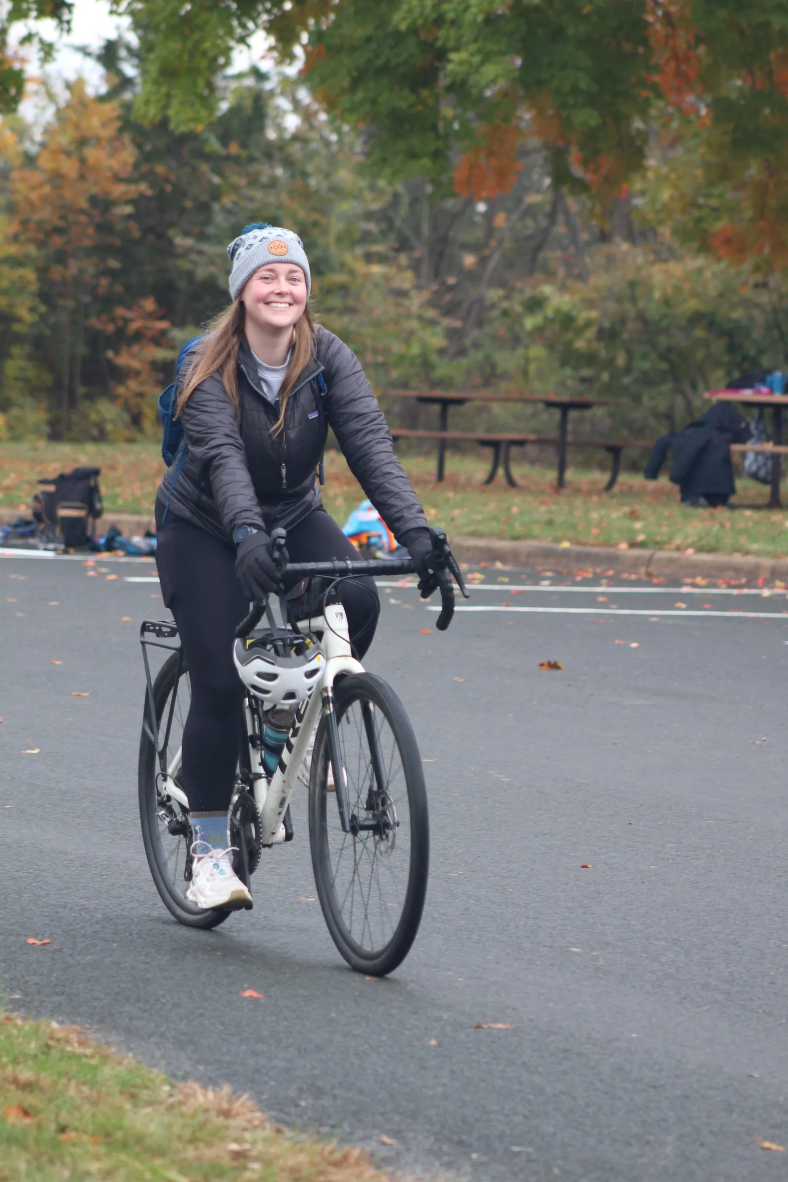 A smiling rider in a beanie on the bike leg of the Dry Tri, fall color behind her