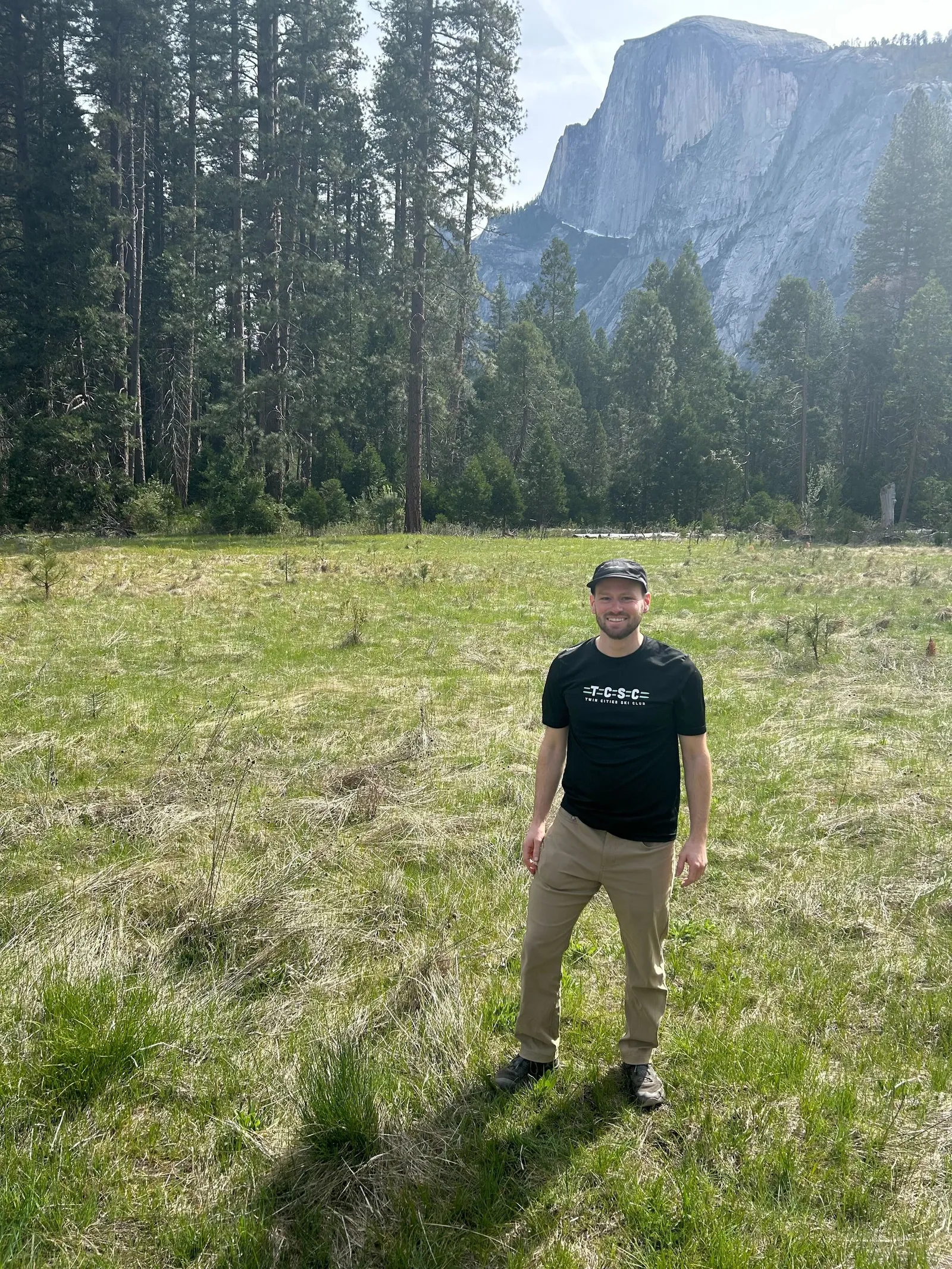 A member in a TCSC tee standing in a Yosemite meadow with Half Dome behind