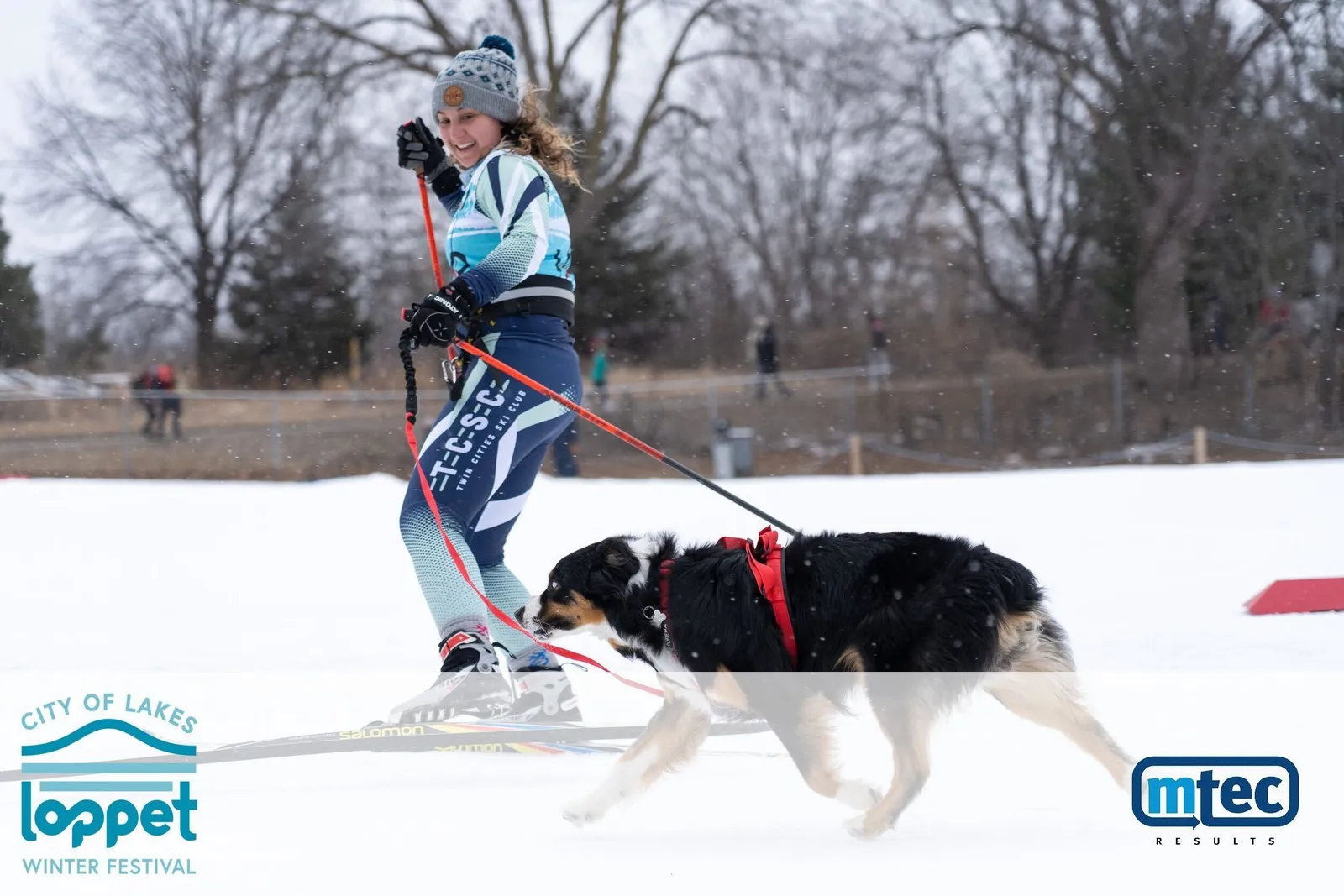 A skier and their dog mid-race at the City of Lakes Loppet skijor, banners lining the course