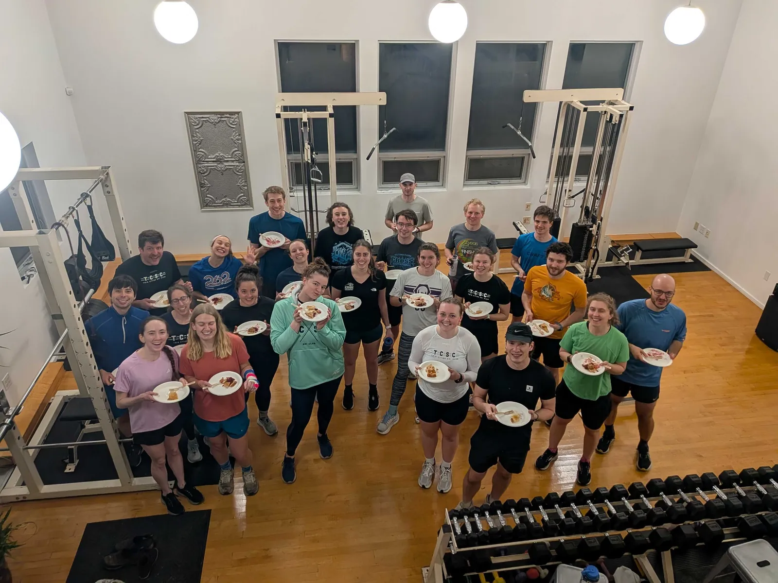 Two dozen members in the gym after strength practice, each holding up a plate of pie