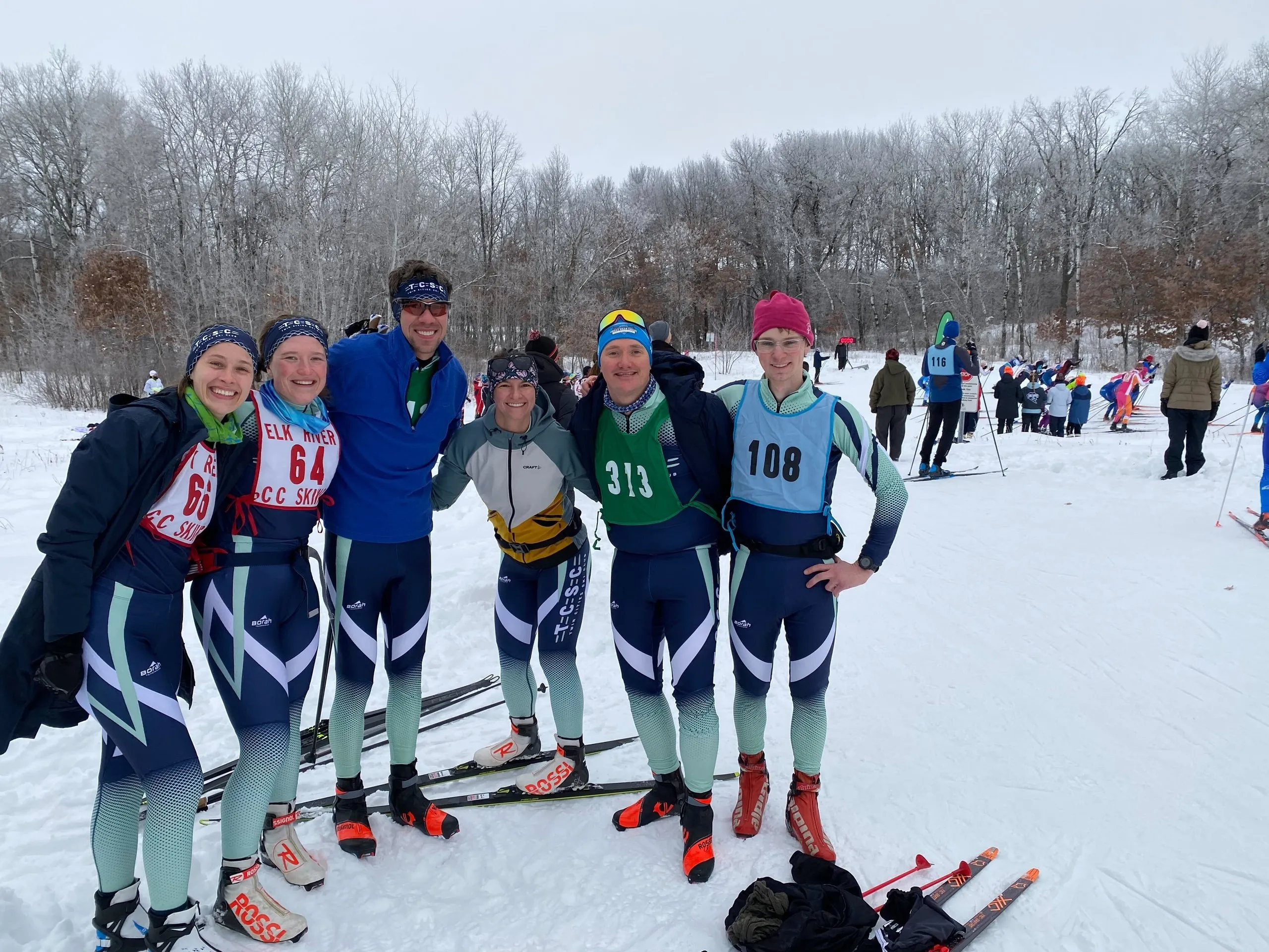 Six members in race bibs, arms around each other, in frosty woods before a start